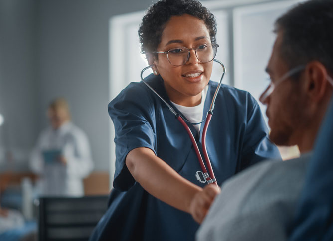 A patient care technician using a stethoscope and talking with a patient.